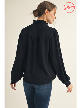 Woman wearing a black blouse with long sleeves and blue jeans on a beige background