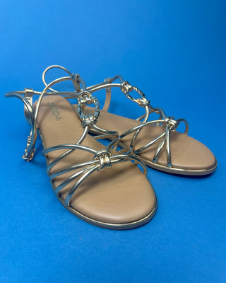 A pair of gold metallic strappy sandals with a tan footbed, against a solid blue background.