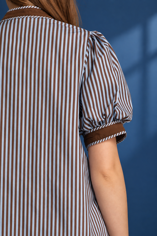 A woman modeling a short-sleeve button-up shirt with vertical blue and white stripes, brown trim
