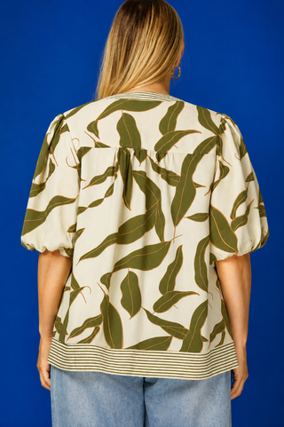 Woman wearing a green leaf-patterned top against a blue background