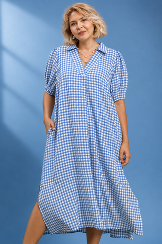 A woman modeling a blue and white gingham midi dress with puff sleeves, a V-neck, and side pockets, set against a blue studio backdrop.