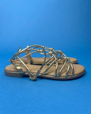 A pair of gold metallic strappy sandals with a tan footbed, against a solid blue background.