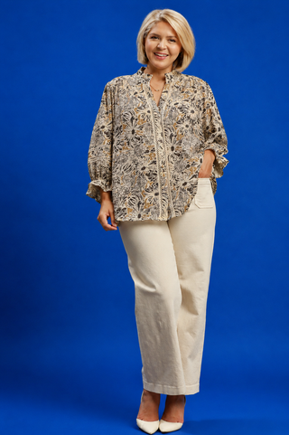 Woman wearing a patterned blouse and beige pants against a blue background