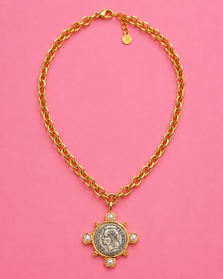 Gold chain necklace with a coin pendant on a pink background
