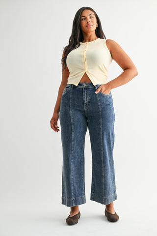 Woman wearing a cream sleeveless top and blue jeans on a white background