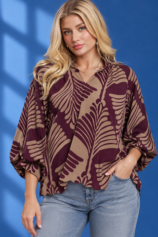 A woman wearing a brown and beige tropical leaf print blouse with balloon sleeves, paired with light blue jeans
