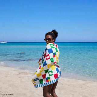 Woman wrapped in a colorful towel on a beach with clear blue water and sky.