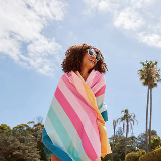 Woman wrapped in a colorful striped towel against a blue sky with palm trees in the background