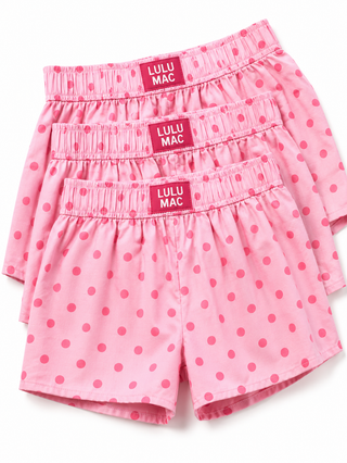 Three pairs of pink children's shorts with darker pink polka dots, stacked together on a white background. Each pair has an elastic waistband with a red label that reads 'LULU MAC'.