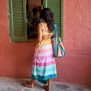 Woman in a colorful striped dress standing in front of a pink wall with green shutters.