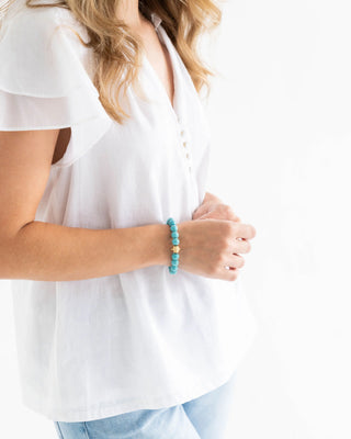 Person wearing a white blouse with a turquoise bracelet on a plain background