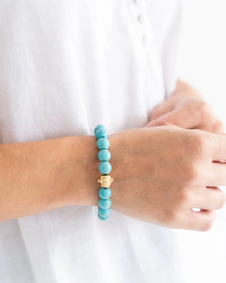 Turquoise beaded bracelet with a gold charm on a wrist against a white background