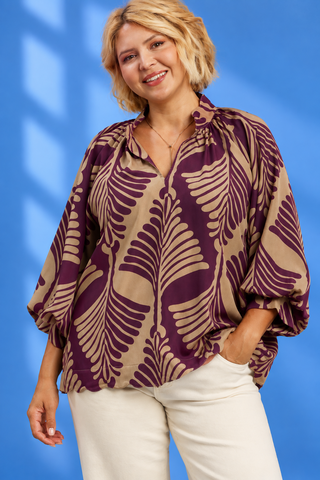 A woman wearing a brown and beige tropical leaf print blouse with balloon sleeves, paired with light blue jeans