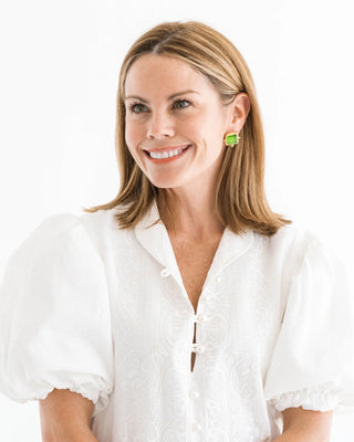 Woman wearing a white blouse with green earrings on a white background