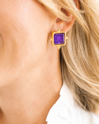 Gold earring with purple gemstone worn by a person with blonde hair.