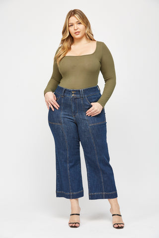 Woman wearing a green long-sleeve top and blue jeans on a white background