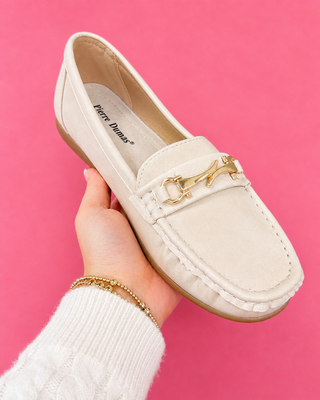 White loafer shoe with gold accent held by a hand against a pink background