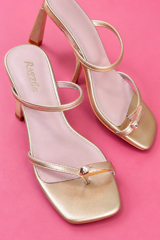 Gold high-heeled sandals with thin straps on a pink background