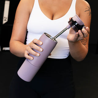 Person holding a purple tumbler with a straw attachment against a dark background