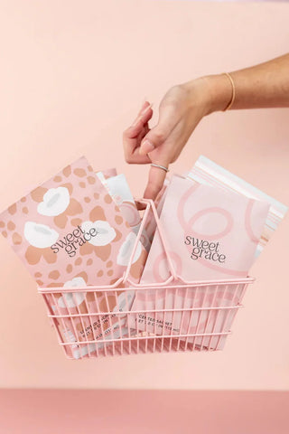 Hand reaching into a basket filled with 'sweet grace' products on a pink background