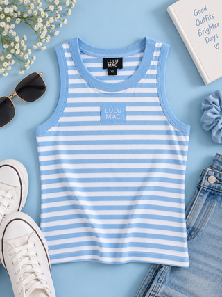 A sleeveless ribbed tank top with light blue and white horizontal stripes, featuring a light blue crew neck and a matching light blue chest patch with 'LULU MAC' text. The tank is styled in a flat lay on a light blue background with white sneakers, sunglasses, a book, and denim jeans.