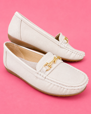 White loafers with gold accents on a pink background