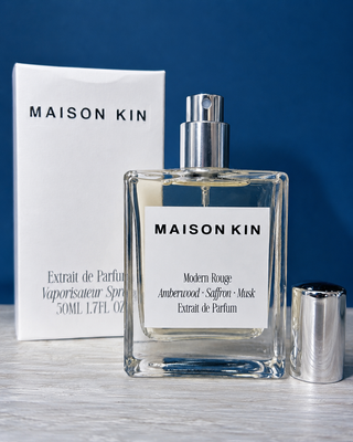 Maison Kin perfume bottle and packaging on a wooden surface with a blue background