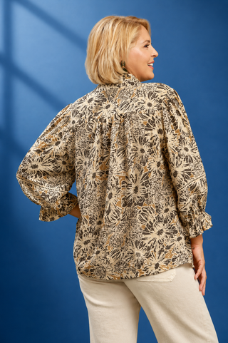 A woman wearing a beige blouse with a black and brown floral pattern, shown from the back against a blue background.
