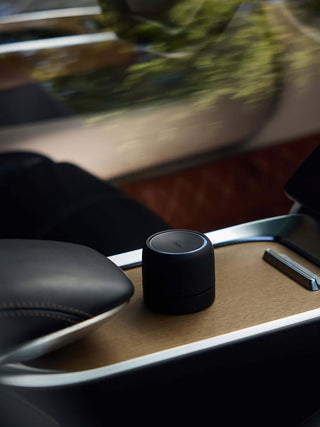 Black cylindrical speaker on a car's tray table with blurred outdoor background