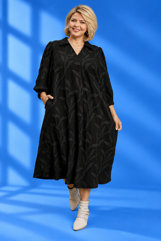 A woman modeling a black midi-length collared dress with a subtle tonal leaf pattern