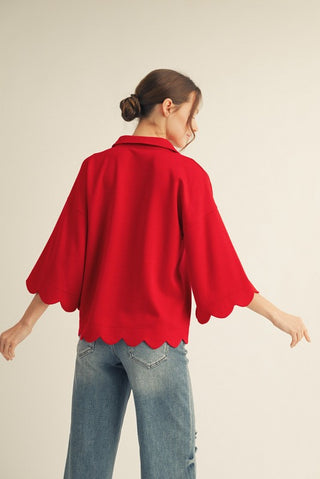 Person wearing a red sweater with scalloped edges and blue jeans on a beige background