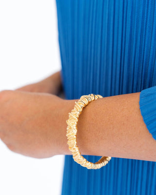 Gold bracelet on a wrist with a blue dress in the background