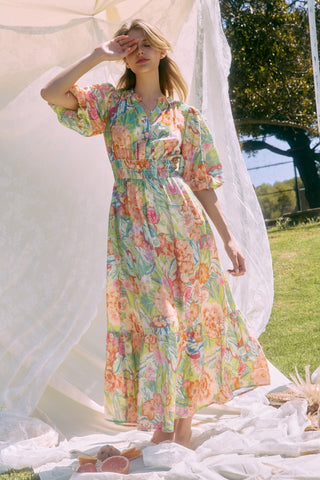 Woman in a floral dress standing outdoors with a white curtain and greenery in the background