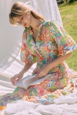 Woman in a floral dress reading a book outdoors.