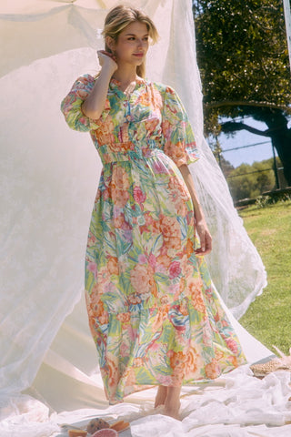 Woman in a floral dress standing outdoors with a white curtain.