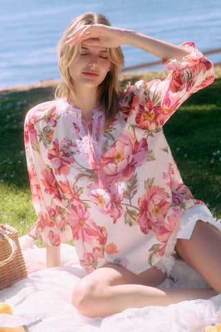 Woman wearing a floral kimono sitting on grass by a body of water.