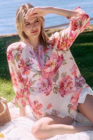 Woman wearing a floral dress sitting on grass by a body of water.