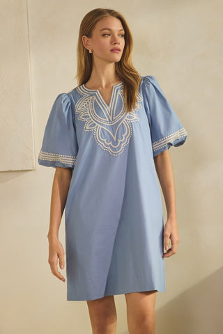 Woman wearing a blue dress with white embroidery on a neutral background