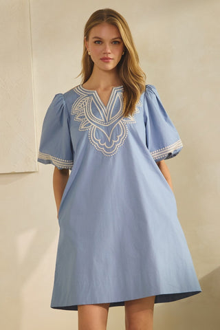 Woman wearing a blue dress with white embroidery against a beige background