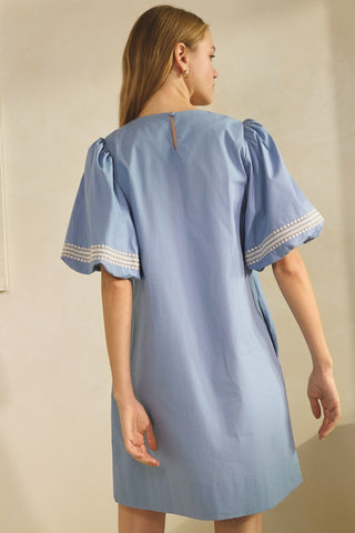 Woman wearing a light blue dress with white trim against a plain background