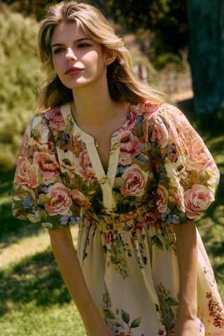 Woman wearing a floral dress standing outdoors with greenery in the background