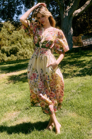 Woman in a floral dress standing in a park with trees and grass.