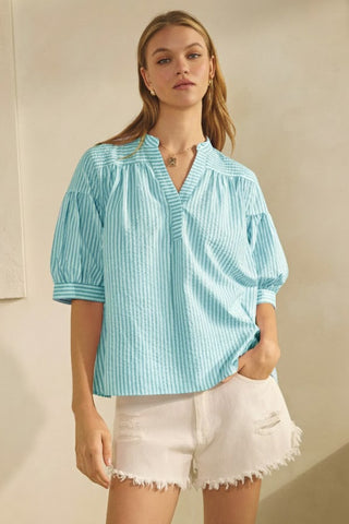 Woman wearing a light blue striped blouse and white shorts against a beige background