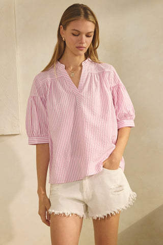 Woman wearing a pink striped blouse and white shorts against a beige background