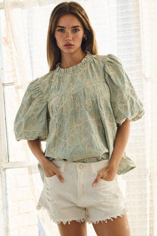 Woman wearing a light green lace blouse and white shorts in a bright room.