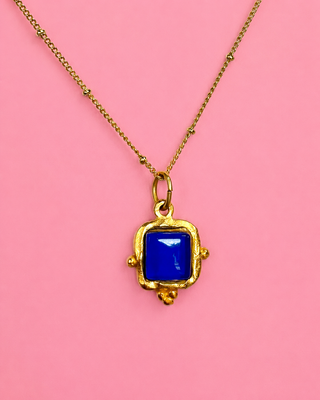 Gold necklace with a blue pendant on a pink background