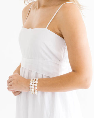Woman wearing a white dress with a close-up of her arm and bracelet on a white background