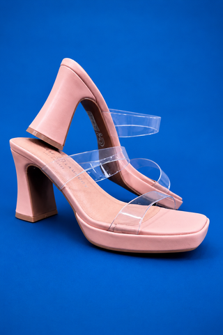A pair of light pink block-heel sandals with transparent plastic straps, displayed on a solid blue background.