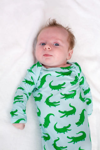 Baby wearing a light blue onesie with green alligator patterns on a white background