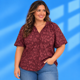 A woman wearing a short-sleeve burgundy top with a tonal leopard print pattern and blue jeans